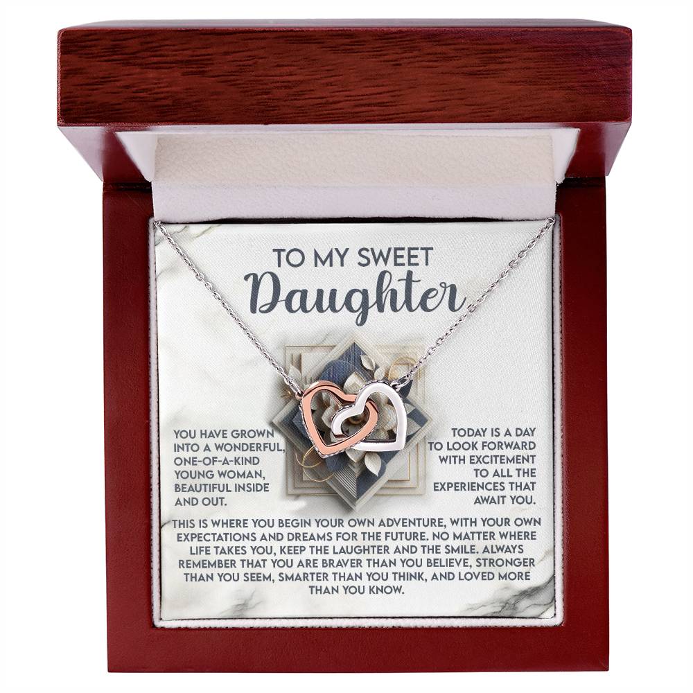 The "Daughter-For The Future - Interlocking Hearts Necklace" features cubic zirconia crystals and comes in a gift box. The lid reads "To My Sweet Daughter," with an inspiring message about growth, adventure, laughter, and strength. Crafted from surgical steel for lasting beauty.