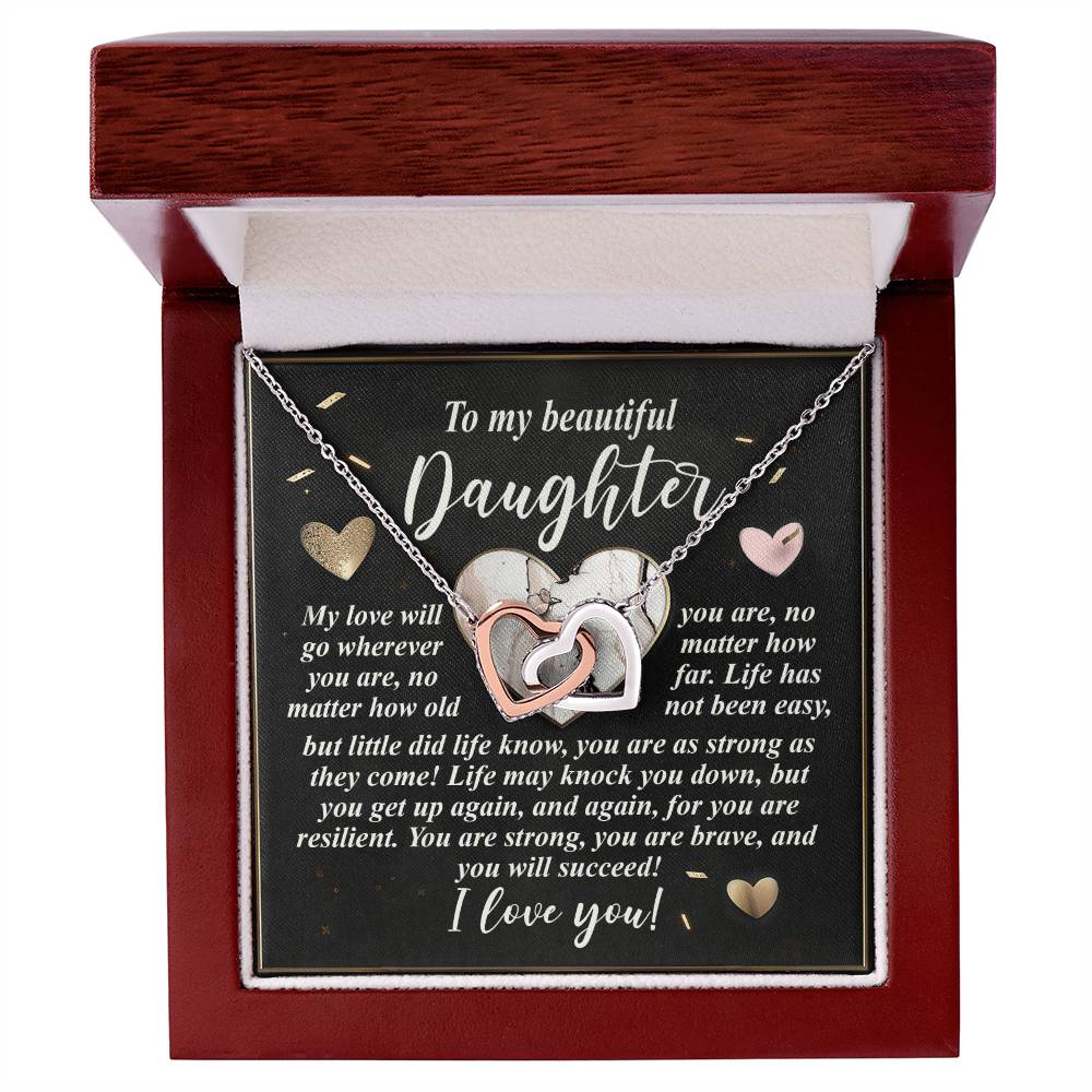 The Daughter-Your Strength Interlocking Hearts Necklace, featuring heart pendants with a silver and rose gold finish adorned with sparkling cubic zirconia crystals, is elegantly presented in a wooden box. Inside, a heartfelt card offers a supportive message about love and resilience to a daughter.