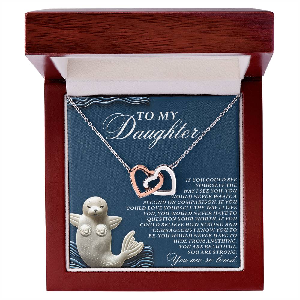 The Daughter-So Loved Interlocking Hearts Necklace features a rose gold finish and comes in a wooden box labeled "To My Daughter." It is adorned with cubic zirconia crystals, with an inscription expressing love and admiration. A white seal figurine enhances its display, highlighting her worth and courage.