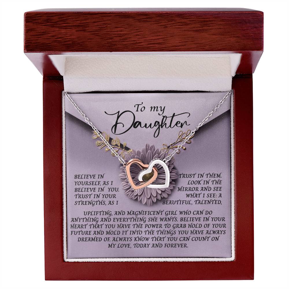 The Daughter-Magnificent Girl - Interlocking Hearts Necklace, with a rose gold finish and cubic zirconia crystals, rests in a wooden jewelry box featuring a heartfelt message about belief, love, and trust in your daughter's talents and future amid elegant floral designs.