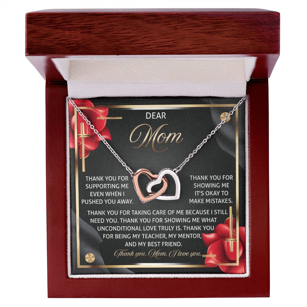 Inside an open jewelry box, the Mom-Best Friend 2 - Interlocking Hearts Necklace in rose gold finish lays beautifully. The lid displays a heartfelt message to "Mom," highlighted by red roses and cubic zirconia crystals, expressing gratitude for her love and support.