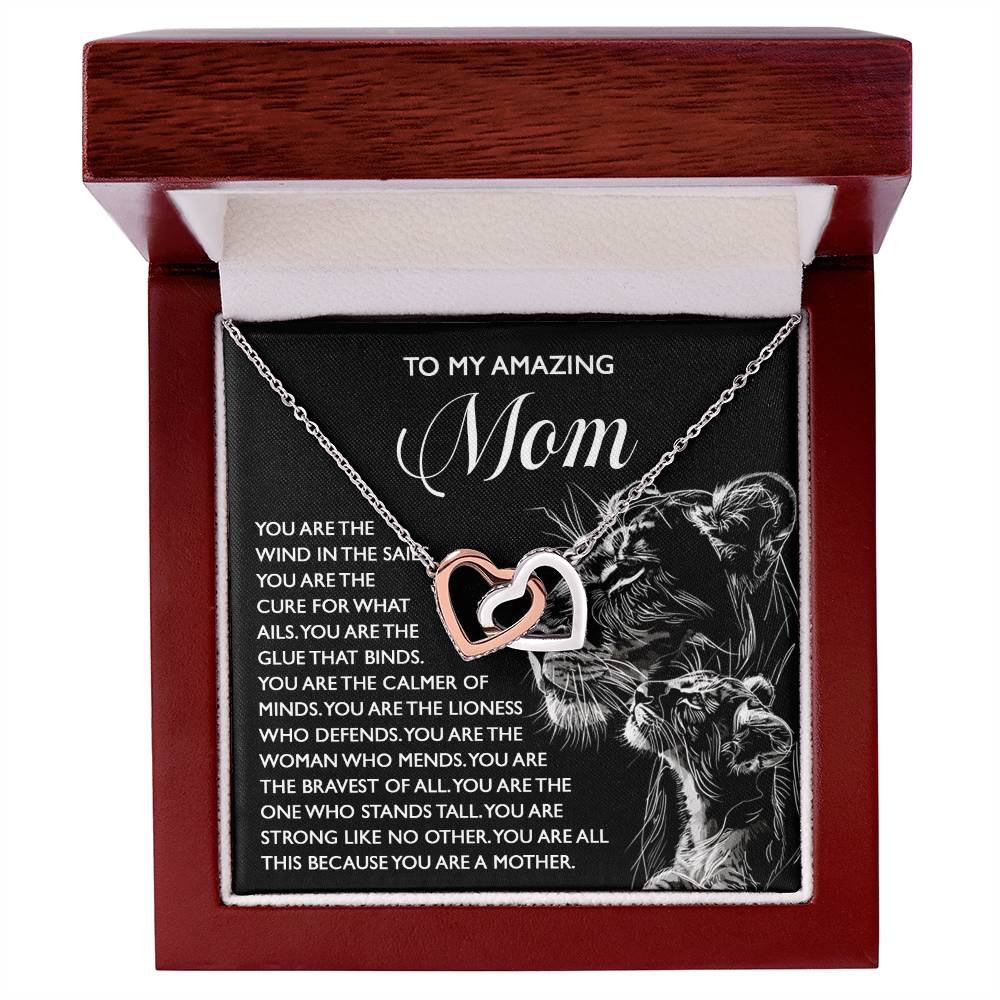 The Mom-The Cure - Interlocking Hearts Necklace, featuring cubic zirconia and a rose gold finish, is showcased in an open red box. A heartfelt message with a lioness and cub motif expresses gratitude, strength, and love for a mother.