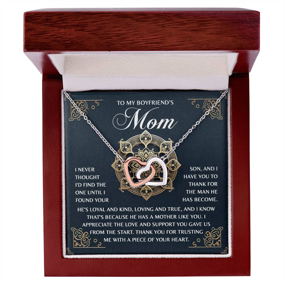 The Mom-Thankful Heart necklace is revealed in a dark wood jewelry box, featuring interlocking hearts with a rose gold finish and shimmering cubic zirconia crystals. The background card reads, "To my boyfriend's mom," expressing deep gratitude for her support and kindness.