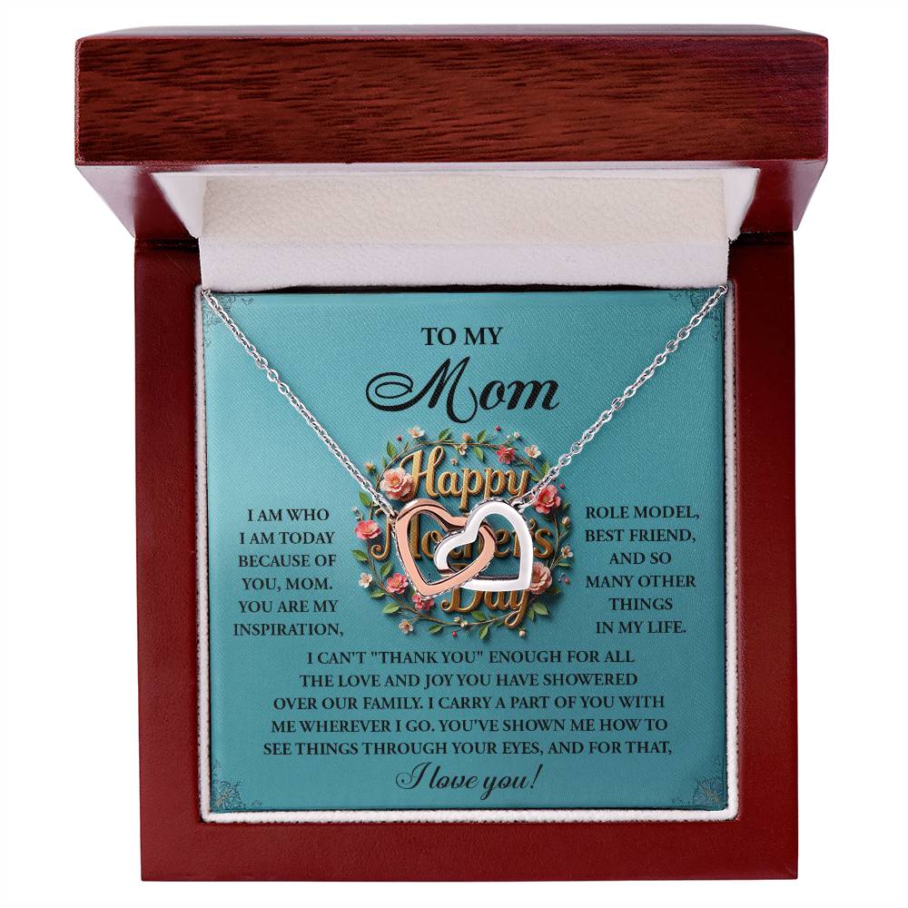 The Mom-Our Family Interlocking Hearts Necklace, featuring a rose gold finish and sparkling cubic zirconia crystals, is displayed in an open wooden box. The teal card backdrop bears a heartfelt message to "Mom," expressing love and gratitude amidst floral decorations.