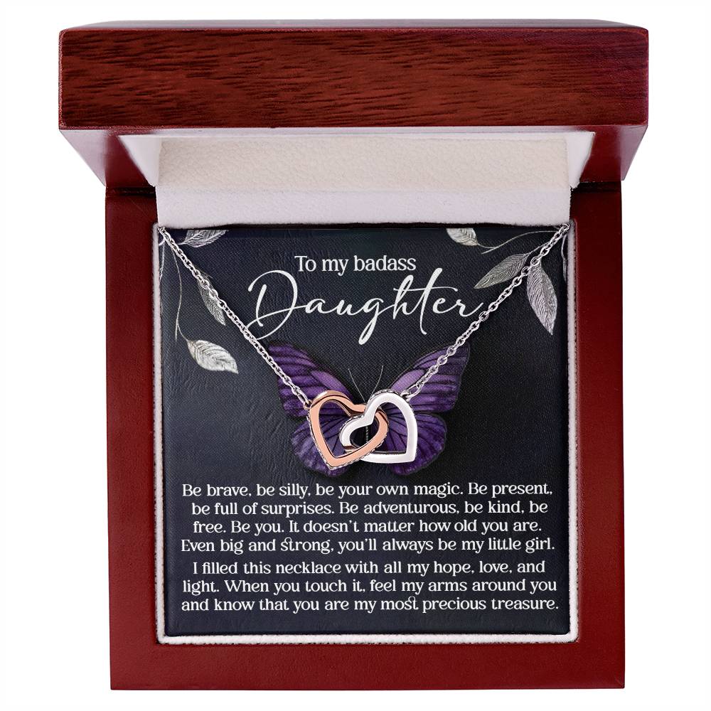 The "Daughter-Big And Strong - Interlocking Hearts Necklace" features a dazzling rose gold finish with cubic zirconia crystals. It comes in a wooden box engraved with "To my badass daughter," encouraging bravery, kindness, and love. The silver and rose gold pendants dangle from a delicate chain.