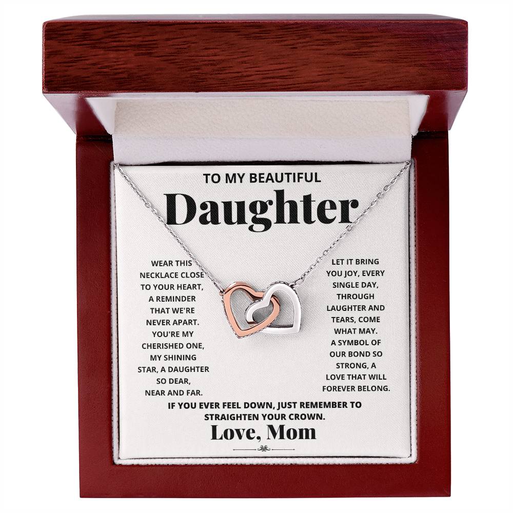 A "To My Beautiful Daughter, Wear This Necklace - Interlocking Hearts Necklace" with interlocking hearts pendants adorned with cubic zirconia crystals, presented in a box with a heartfelt message from a mother to her daughter.