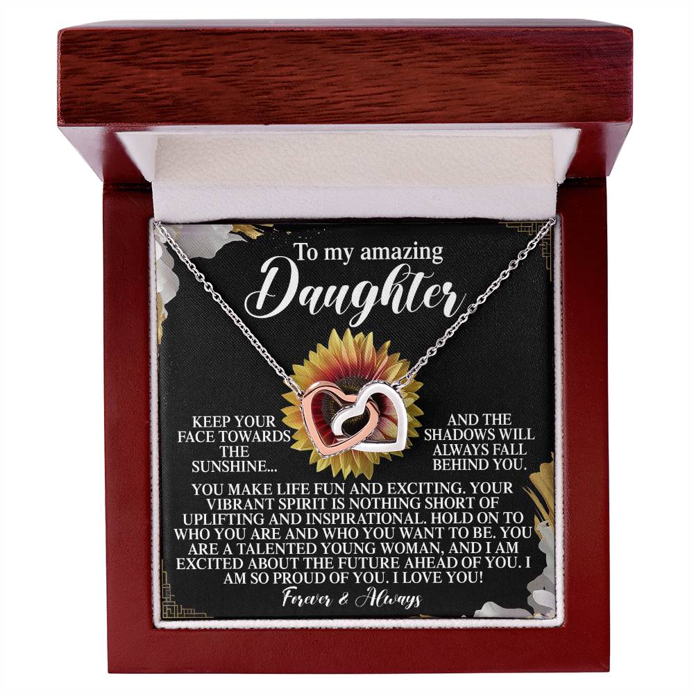 A jewelry gift box contains the Daughter-Vibrant Spirit Interlocking Hearts Necklace with cubic zirconia crystals and a rose gold finish, set against sunflowers and a heartfelt message to a daughter, conveying pride, love, and encouragement to remain positive.