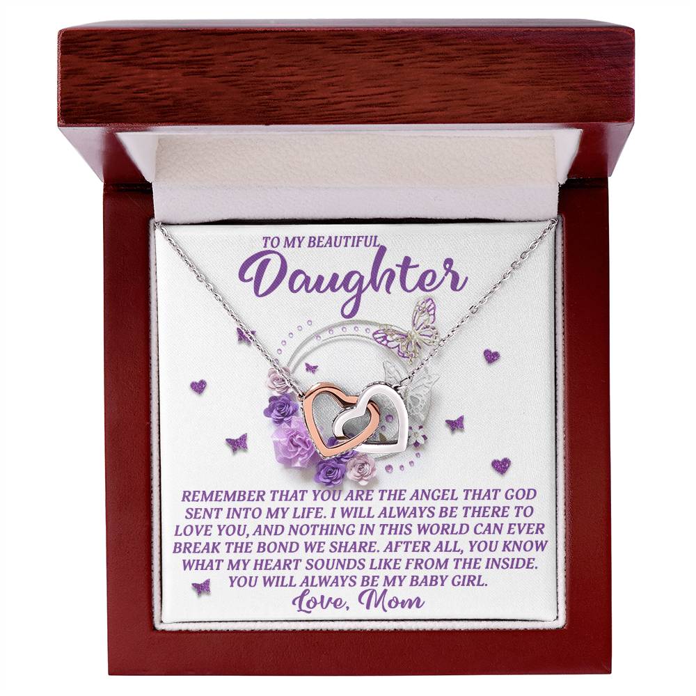 The Daughter-Angel Heart necklace, featuring a rose gold finish and cubic zirconia crystals, is presented in a wood box with the message, "To my beautiful daughter, remember that you are the angel that God sent into my life... Love, Mom," against a backdrop of flowers and butterflies.
