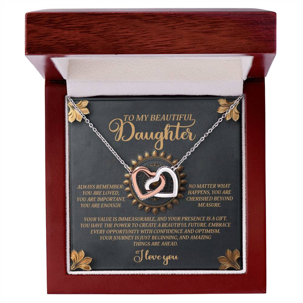 The Daughter-Beautiful Future Interlocking Hearts Necklace, in a wooden box, showcases a cubic zirconia-adorned heart pendant. The lid features heartfelt gold and white text on a dark background, complementing the necklace's rose gold finish.