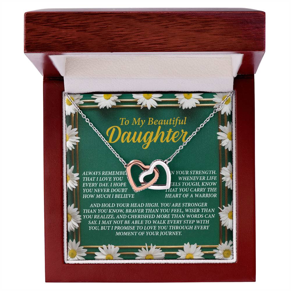 The Daughter-Your Journey Interlocking Hearts Necklace in a rose gold finish is elegantly showcased in an open wooden box. A floral backdrop and heartfelt message emphasize strength, love, and support, while sparkling cubic zirconia crystals adorn the necklace.