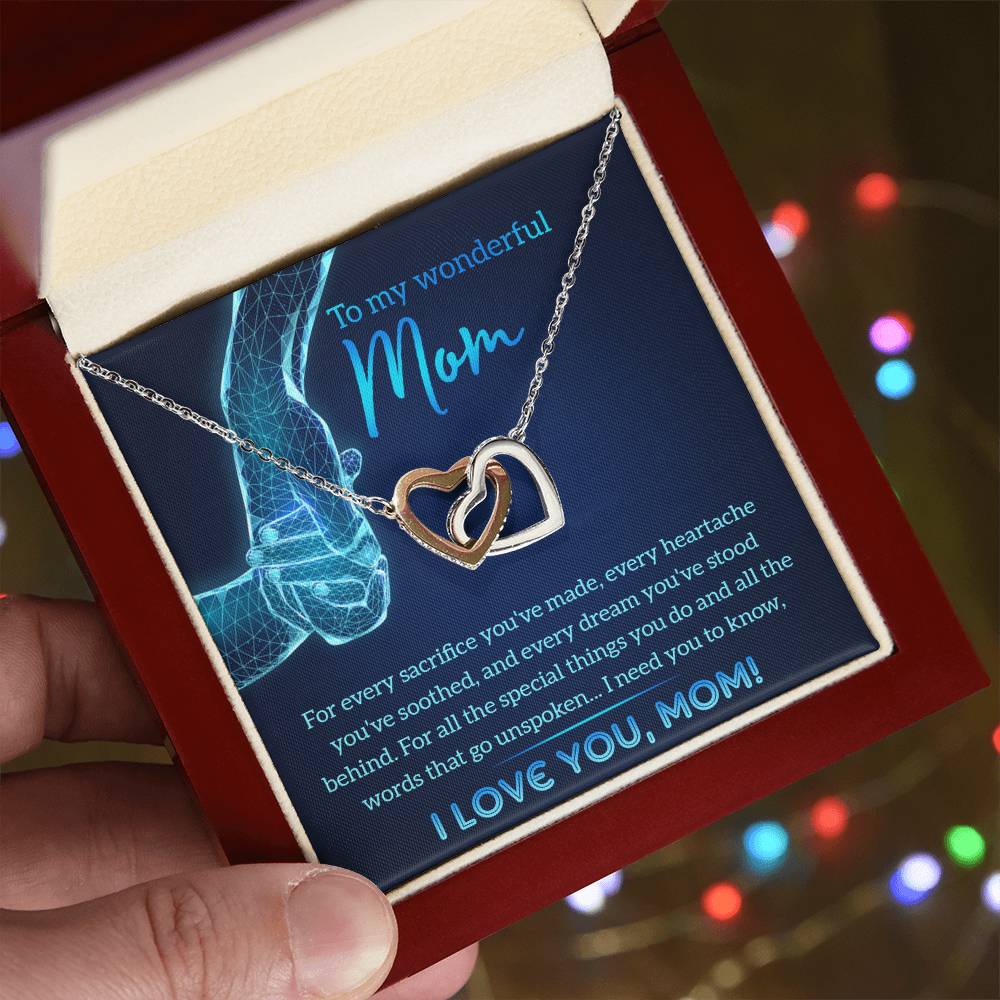 A hand holds an open jewelry box displaying the "To Mom, Stood Behind - Interlocking Hearts Necklace" with cubic zirconia crystals. Inside, it reads: "To my wonderful Mom... I love you, Mom!" adding a heartfelt touch to this personalized gift.