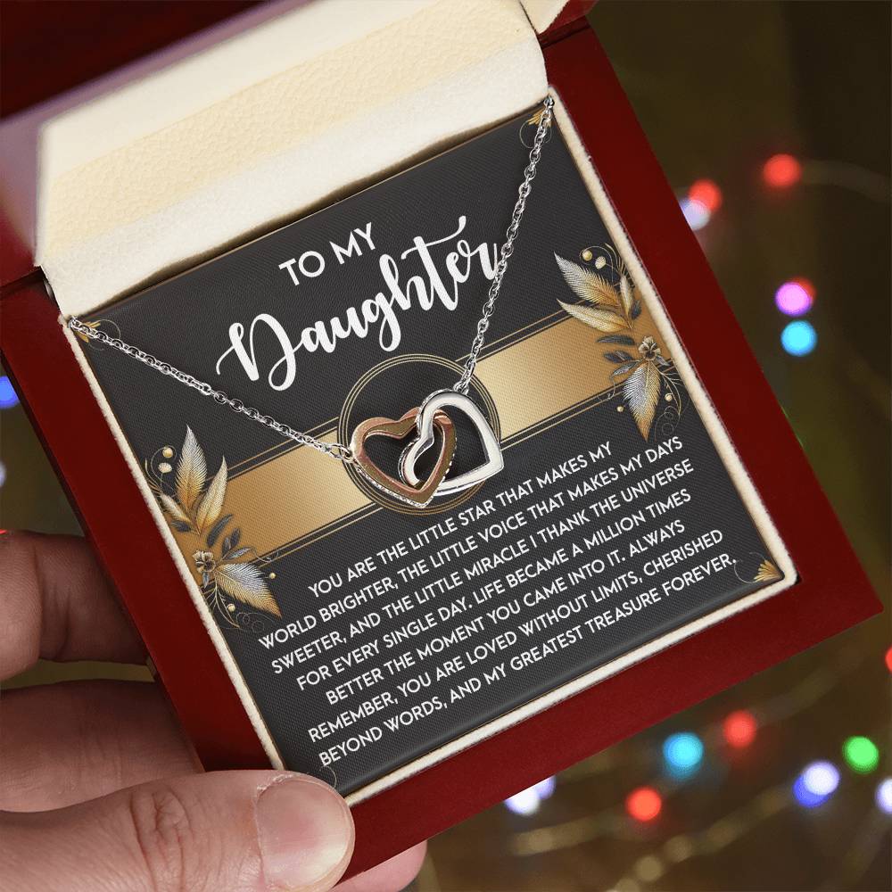 A hand displays an open jewelry box with the "Daughter-Greatest Treasure - Interlocking Hearts Necklace" adorned with cubic zirconia. Blurred colorful lights and a heartfelt message card addressed to a daughter create the perfect gift for her.