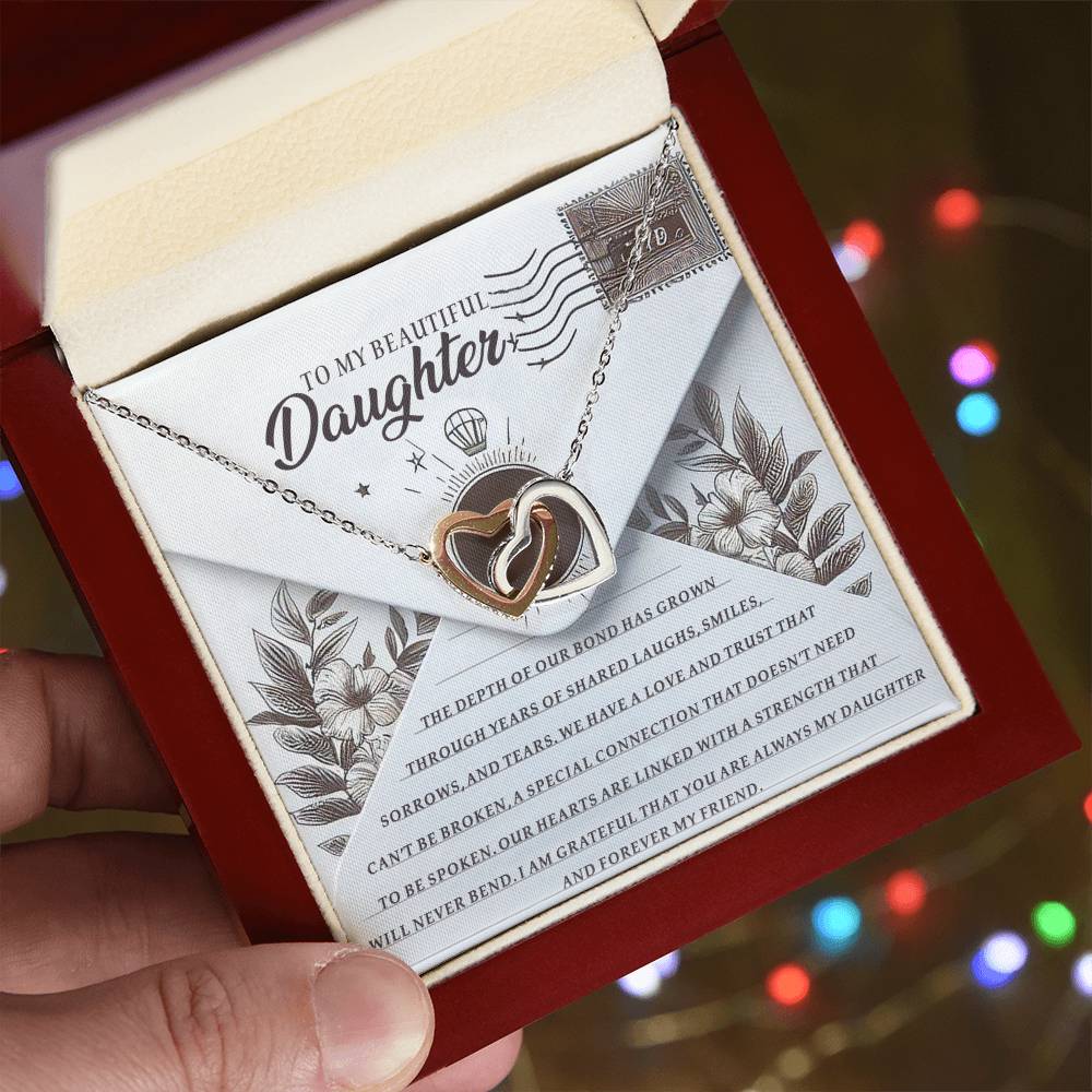 A hand presents an open red box containing the Daughter-My Friend - Interlocking Hearts Necklace with cubic zirconia crystals. The box lid says "TO MY BEAUTIFUL Daughter," with a heartfelt message visible against a blurred colorful background.