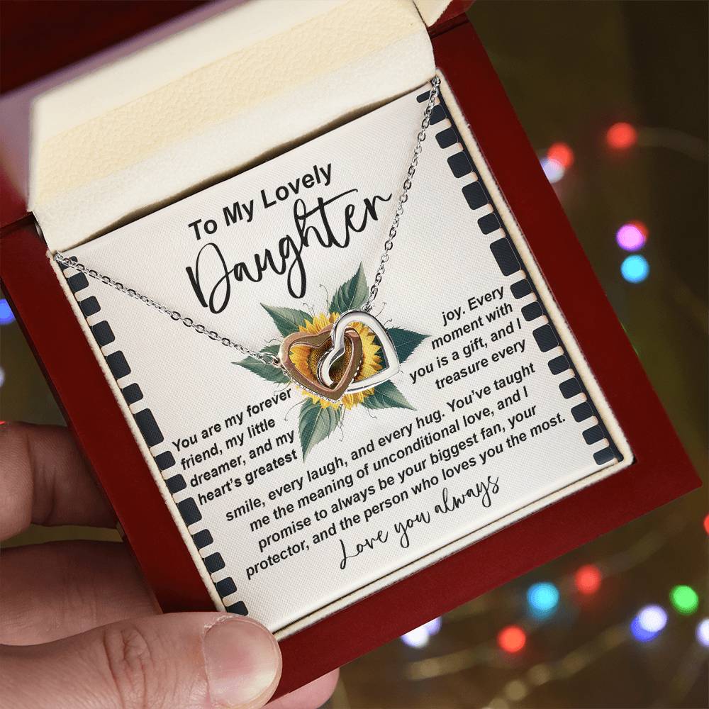 A hand displays an open jewelry box with the "Daughter-Little Dreamer" Interlocking Hearts Necklace, adorned with cubic zirconia. A heartfelt message card for a daughter adds warmth, while a rose gold finish boosts its elegance against blurred lights.