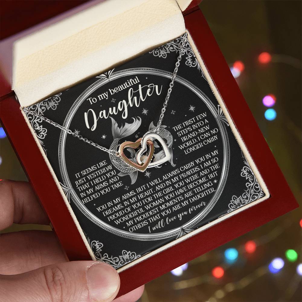 A hand holds an open red jewelry box, displaying the Daughter-In My Prayers - Interlocking Hearts Necklace adorned with cubic zirconia crystals and an infinity symbol. A heartfelt message to a daughter is in the background, with soft, colorful lights blurred in the distance.