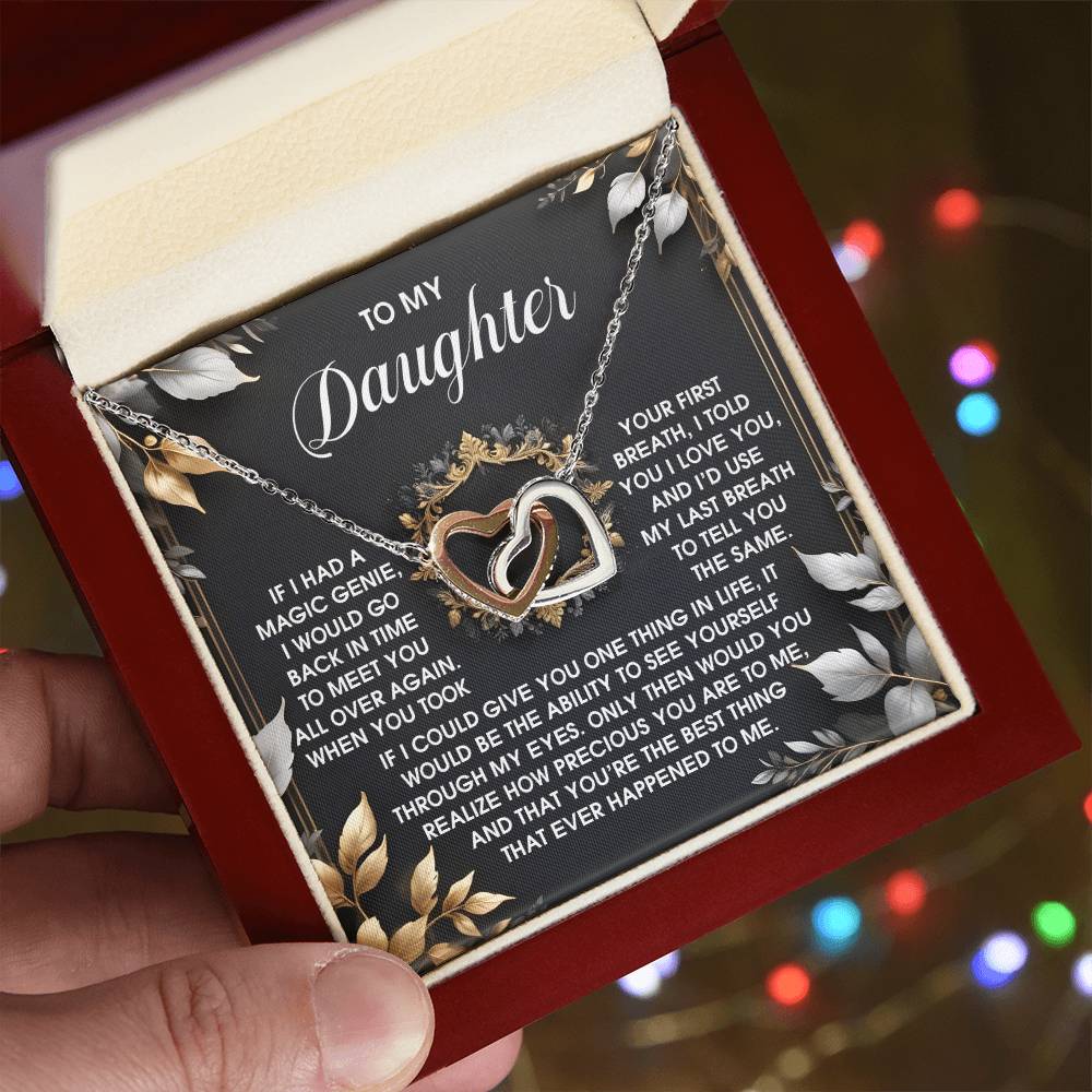 A hand displays an open red jewelry box with the "Daughter-Over Again" Interlocking Hearts necklace, crafted from surgical steel and adorned with cubic zirconia. The box background features a heartfelt message for a daughter.