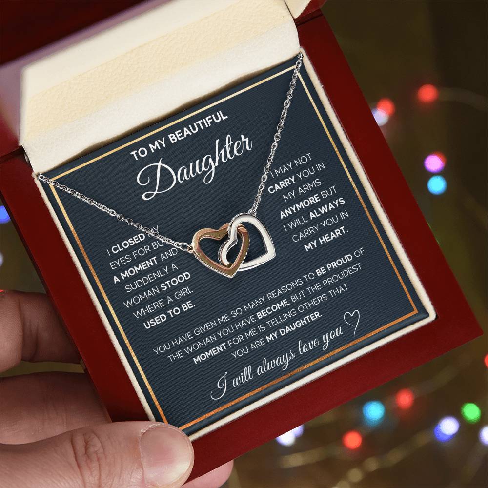 Person holding an anniversary gift box with a heartfelt message and a To My Daughter, I Will Always Carry You In My Heart - Interlocking Hearts Necklace adorned with cubic zirconia crystals for a daughter from ShineOn Fulfillment.