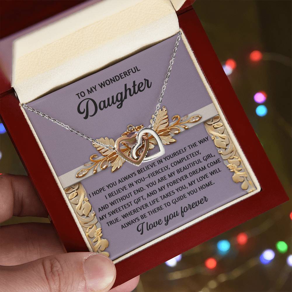 A hand presents an open box revealing the Daughter-Guide You Home - Interlocking Hearts Necklace. Crafted with a rose gold finish and cubic zirconia crystals, it is accompanied by a heartfelt message in a lid that begins with "To my wonderful daughter" and ends with "I love you forever," set against colorful lights.