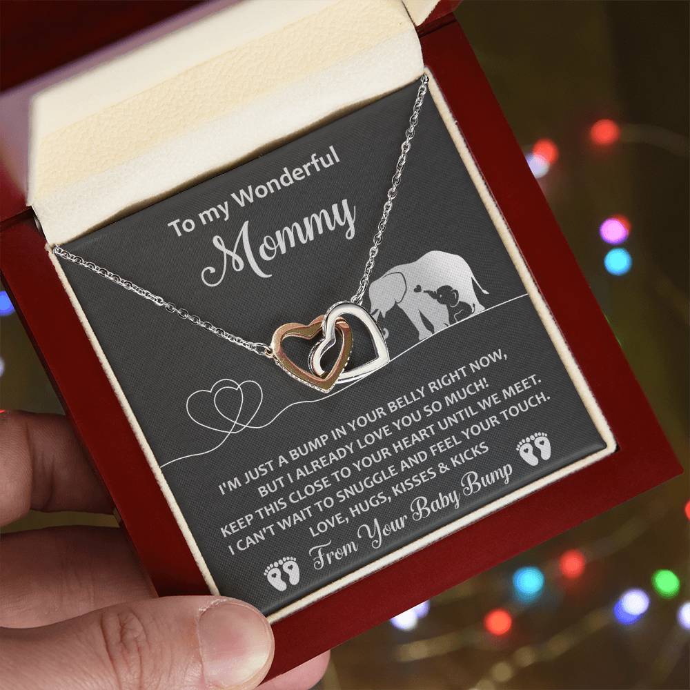 A hand holds an open jewelry box showing a "To Mama To Be, Until We Meet - Interlocking Hearts Necklace" with cubic zirconia crystals. The box reads, "To my Wonderful Mommy" – a unique gift featuring a heartfelt message from "Your Baby Bump.