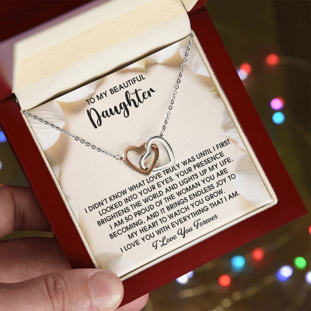 A hand holds an elegant necklace box, unveiling the Interlocking Hearts Necklace with a rose gold finish and sparkling cubic zirconia. Inside the lid, a heartfelt message is etched, expressing profound love and appreciation to a cherished daughter.