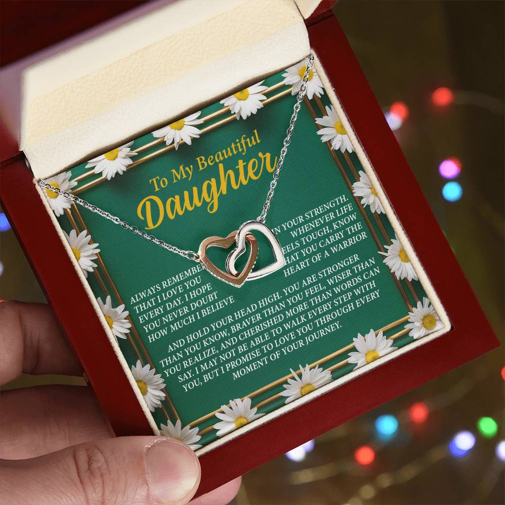 An open jewelry box held in a hand displays the dazzling Daughter-Your Journey - Interlocking Hearts Necklace with a rose gold finish. Decorated with daisy illustrations, the box features the message: "To My Beautiful Daughter" and a heartfelt note, against colorful background lights.