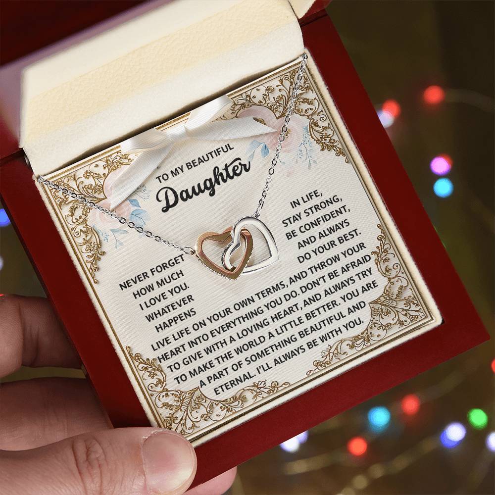A person holds an open jewelry gift box containing the "Daughter-Beautiful And Eternal - Interlocking Hearts Necklace," featuring a sentimental message, elegantly finished in 18k yellow gold and adorned with shimmering cubic zirconia crystals.