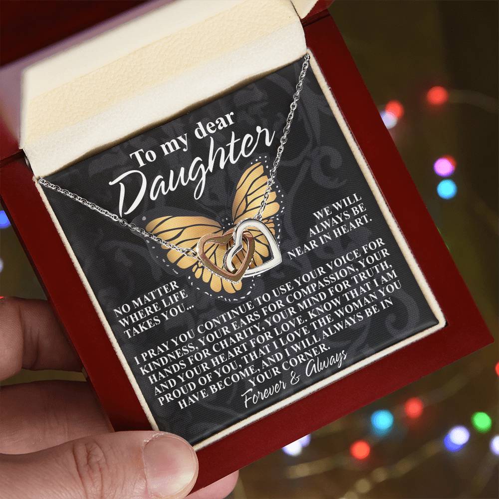 The "Daughter-In Your Corner" Interlocking Hearts Necklace, with a rose gold finish, comes in a gift box featuring a heartfelt message. The background, adorned with bokeh lights and cubic zirconia crystals, creates a warm festive atmosphere.