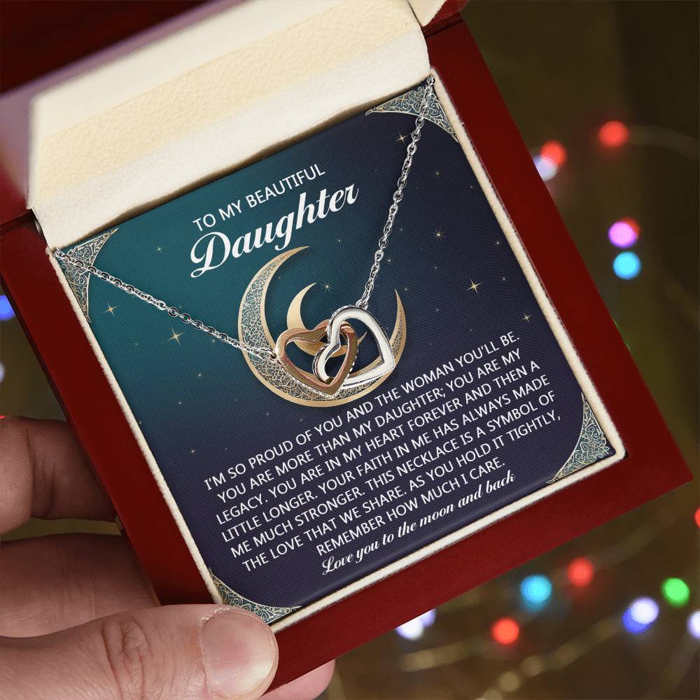 A hand holds an open red jewelry box containing the dazzling Daughter-Hold It Tightly - Interlocking Hearts Necklace, adorned with sparkling cubic zirconia crystals. The box's lid shares a heartfelt message to "Daughter," surrounded by blurred, colorful lights in the background.