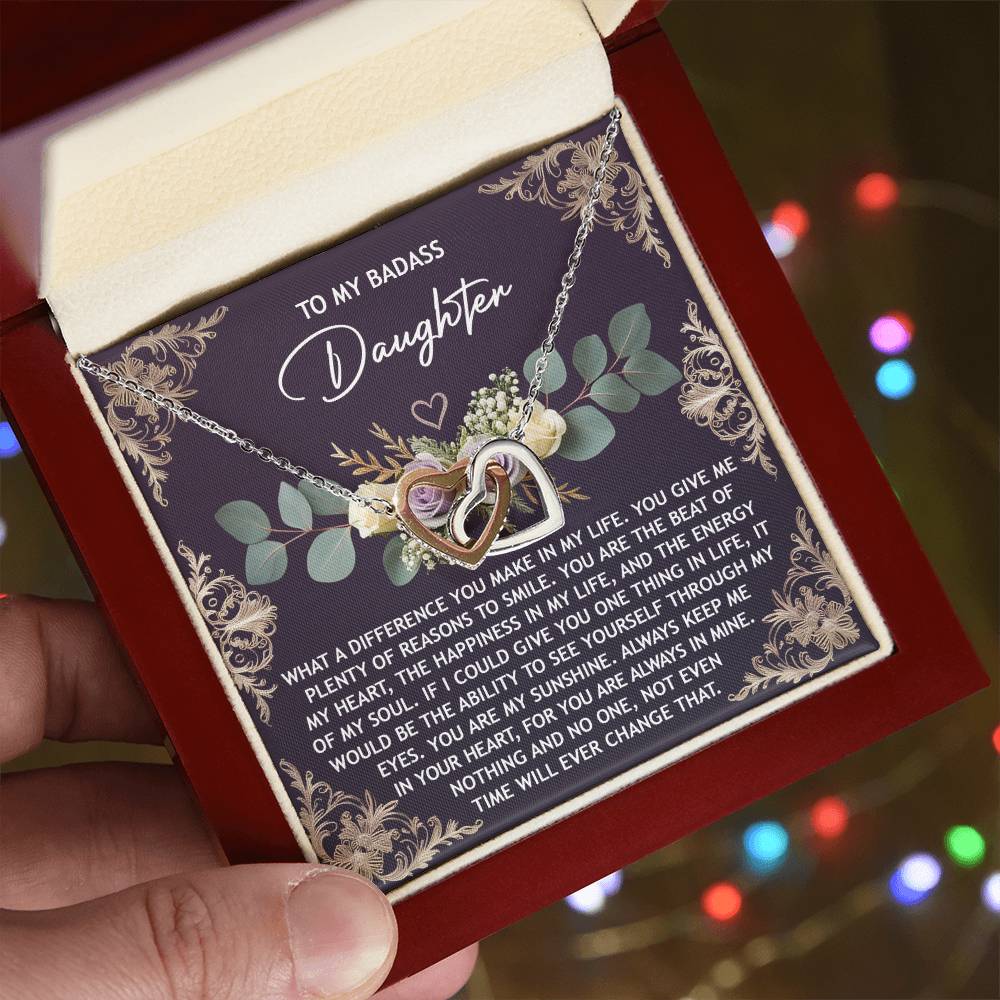 A hand presents an open jewelry box displaying the Daughter-Always In Mine - Interlocking Hearts Necklace on a card with a heartfelt message. Adorned with shimmering cubic zirconia, it's an unforgettable gift for your daughter.