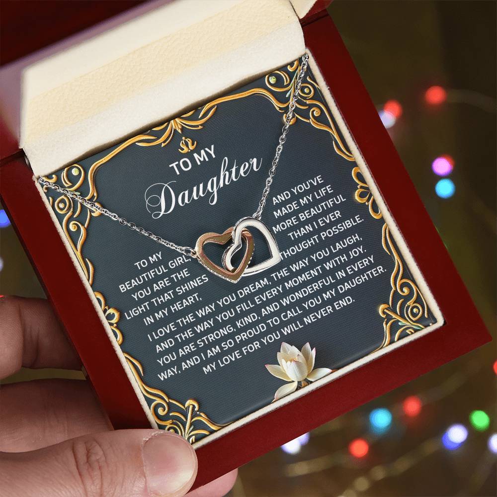A person holds the Daughter-Never End - Interlocking Hearts Necklace, featuring a rose gold finish and cubic zirconia crystals, in a gift box. It includes a heartfelt message to a daughter framed by an elegant decorative gold border.