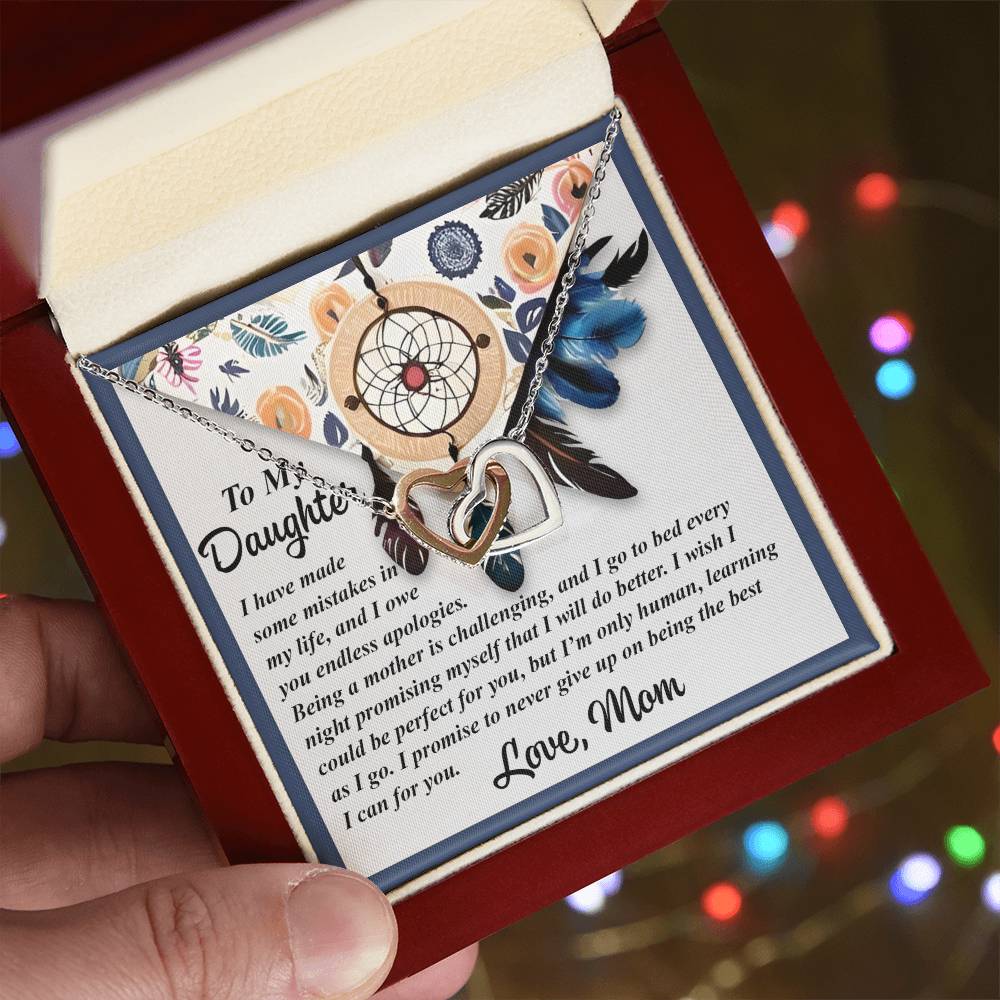 A hand holds an open jewelry box with a rose gold finish, revealing the Daughter-For You - Interlocking Hearts Necklace adorned with cubic zirconia crystals. The accompanying card shares a heartfelt message from a mother to her daughter, expressing love and encouragement.