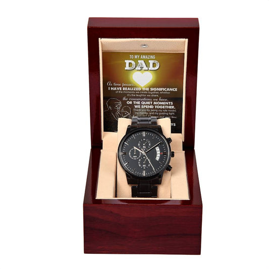 A black chronograph wristwatch presented in an open wooden gift box with a "To Dad, My Guiding Light" message displayed inside the lid.