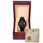 A black To Husband, Great Father - Metal Chronograph Watch with a copper dial is displayed in an open wooden box lined with beige fabric. Behind the watch, an illustrated card with text is positioned upright within the box.