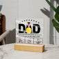 A framed acrylic plaque with the word "DAD" and a gold medal sits elegantly on an LED wooden base. Text underneath reads, "To the world, you may be just one person, but to me, you are the whole world," above three hand-drawn images of hands. A perfect sentimental gift for any father. This is the To Dad, The Whole World - Acrylic Square Plaque.