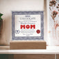 The "To Mom, World's Greatest Mom" acrylic square plaque, elegantly displaying a certificate with a decorative border and red seal, is beautifully showcased on an LED wooden base that adds a warm glow.