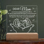 This acrylic plaque, titled "To Mom, Your Little One," showcases hands cradling baby feet and a loving message. Elegantly placed on a wooden base with LED lights, it is the perfect Mother's Day gift from daughter or son.