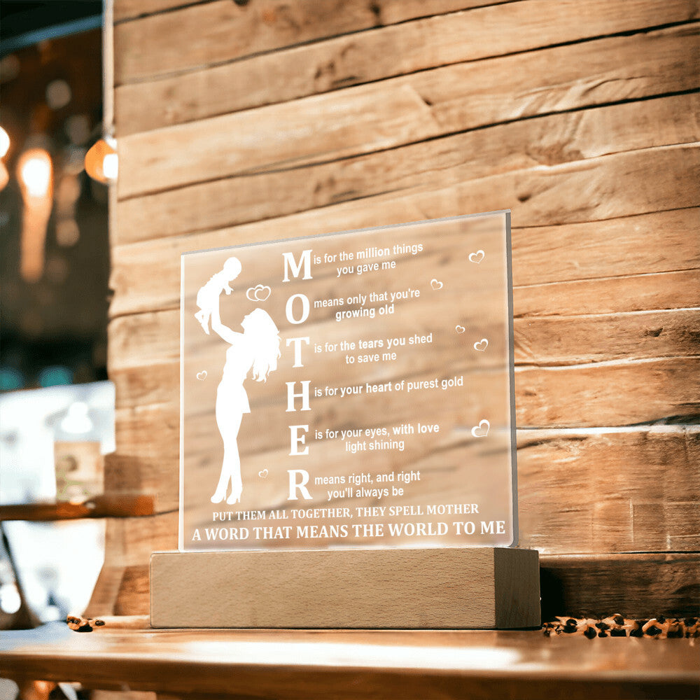 A Mother Acronym Acrylic Plaque with a poem about a mother, featuring a silhouette of a mother and child, displayed on a wooden stand against a plant backdrop—perfect as a Mother's Day gift.