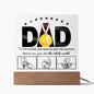 A framed acrylic plaque with the word "DAD" and a gold medal sits elegantly on an LED wooden base. Text underneath reads, "To the world, you may be just one person, but to me, you are the whole world," above three hand-drawn images of hands. A perfect sentimental gift for any father. This is the To Dad, The Whole World - Acrylic Square Plaque.