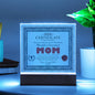 A framed To Mom, World's Greatest Mom Acrylic Square Plaque titled "certificate of achievement", with decorative borders, a seal, and signatures, standing on an LED wooden base.
