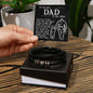 A hand presenting an open gift box containing the To Dad, By My Side - Love You Forever Bracelet and a card with a heartfelt message for 'the best dad in the world'.