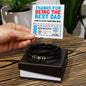 Hands holding a "To Dad, Gift Voucher - Love You Forever Bracelet" above a black vegan leather bracelet with decorative metal accents, in a box.