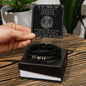 A hand holding a card with a message "To My Viking Dad" above a black vegan leather braided men's bracelet with metal beads and an engraved message in an open box.