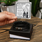 A hand holds a card reading "To My Husband" with a heartfelt message. Below the card, a stylish men's bracelet made of vegan leather with metallic accents and an engraved message rests in a box: the "To My Husband, I Am Yours - Love You Forever Bracelet.