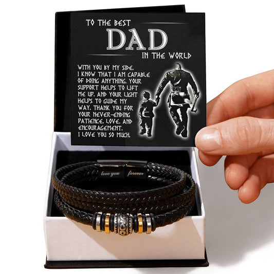 A hand presenting an open gift box containing the To Dad, By My Side - Love You Forever Bracelet and a card with a heartfelt message for 'the best dad in the world'.