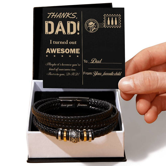 A hand is holding a card that reads "Thanks, Dad! I turned out awesome" above a To Dad, Kind Of Awesome - Love You Forever Bracelet, placed inside a white and black gift box.