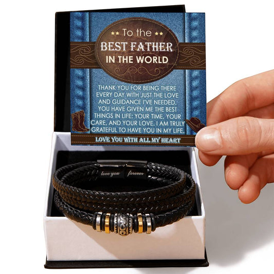 A hand holding a card that reads "To the Best Father in the World," above a black braided leather bracelet with metal accents, the perfect sentimental gift. This "To Dad, All My Heart - Love You Forever Bracelet" comes elegantly packaged in a stylish gift box.