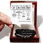 A hand holding a periodic table-inspired card with a humorous "FATHER" message. Below the card, an engraved men's bracelet made of black braided leather with metallic accents, labeled "To Father, Still The Best - Love You Forever Bracelet," is displayed in an open gift box.