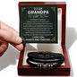 A hand holds a card that reads "To My Grandpa" above a decorative message. Below the card is a black vegan leather bracelet with metal accents in a white box—an ideal engraved gift for any special man, the "To Grandpa, Thank You - Love You Forever Bracelet.