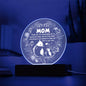A translucent circular glass plate with a leaf pattern at the edges, displayed upright on a wooden LED base against a white background.