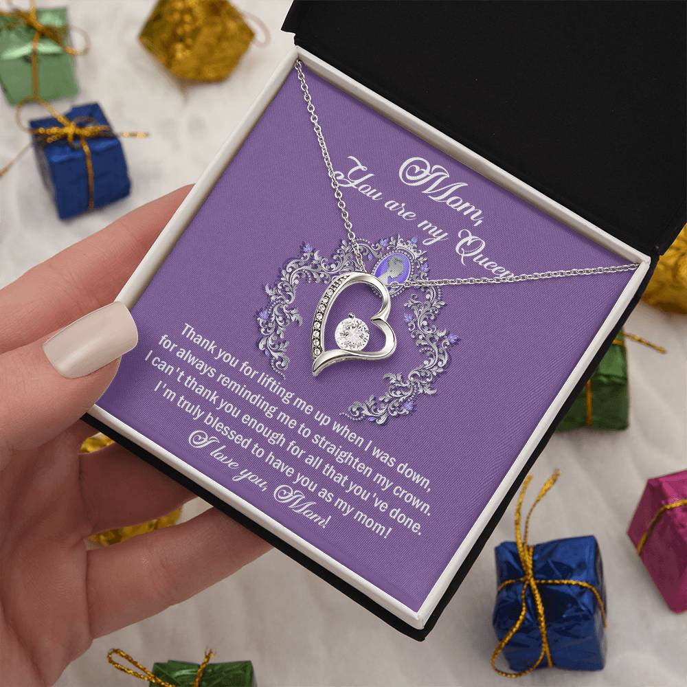 A person holds a purple box containing the "To Mom, Belongs To Me - Forever Love Necklace," along with a note that reads, "Mom, you are my Queen. Thanks for always being there. I'm truly blessed to have you as my mom. Love, your child.